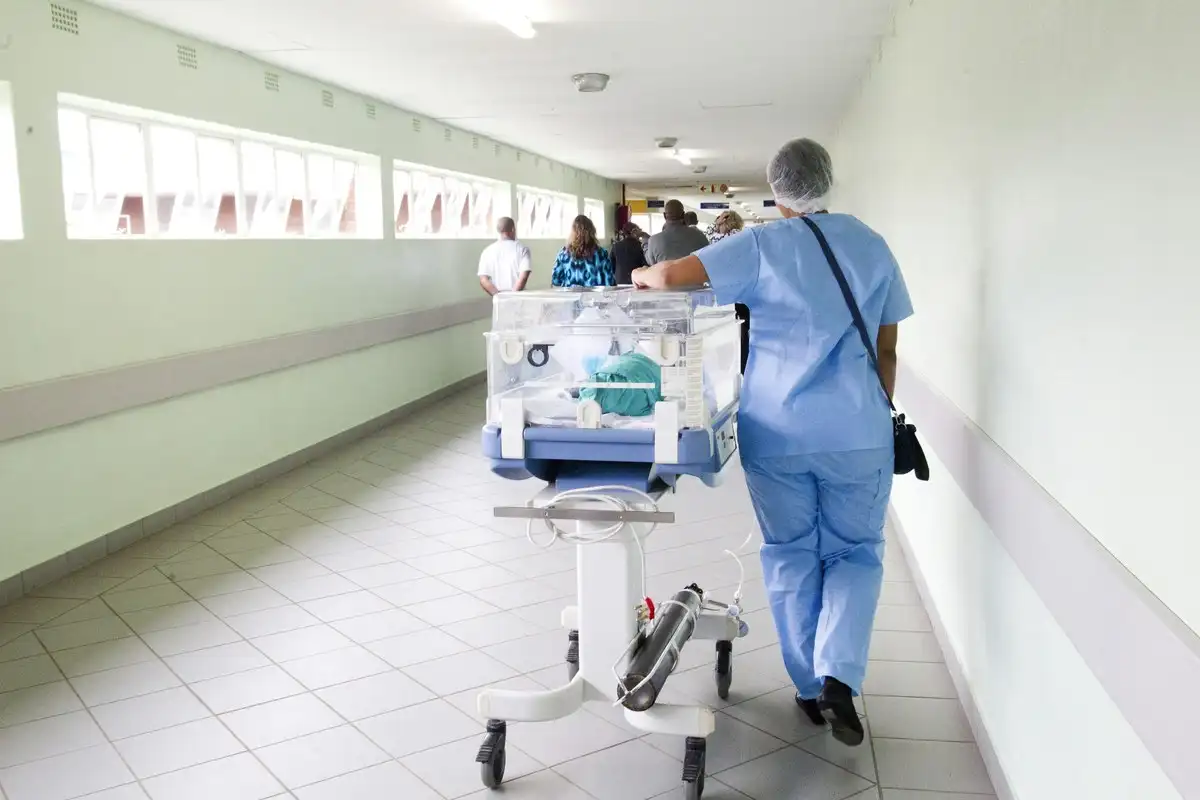 Pasillo de hospital con personal sanitario trasladando una incubadora